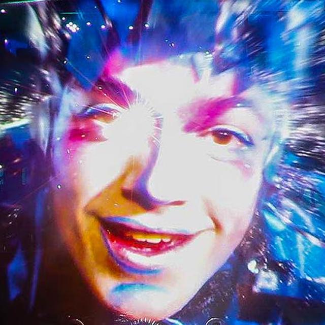 Close-up of a Cirque du Soleil performer’s face projected on a giant screen with vibrant digital effects and dramatic lighting.