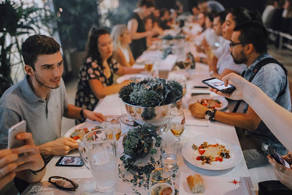 Guests share a communal dining experience at a long table during a Cirque du Soleil immersive dinner event, with plated dishes and table décor.