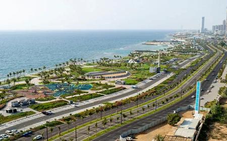 Aerial view of Jeddah’s coastal corniche with seaside roads, green spaces, and the Red Sea in the background.