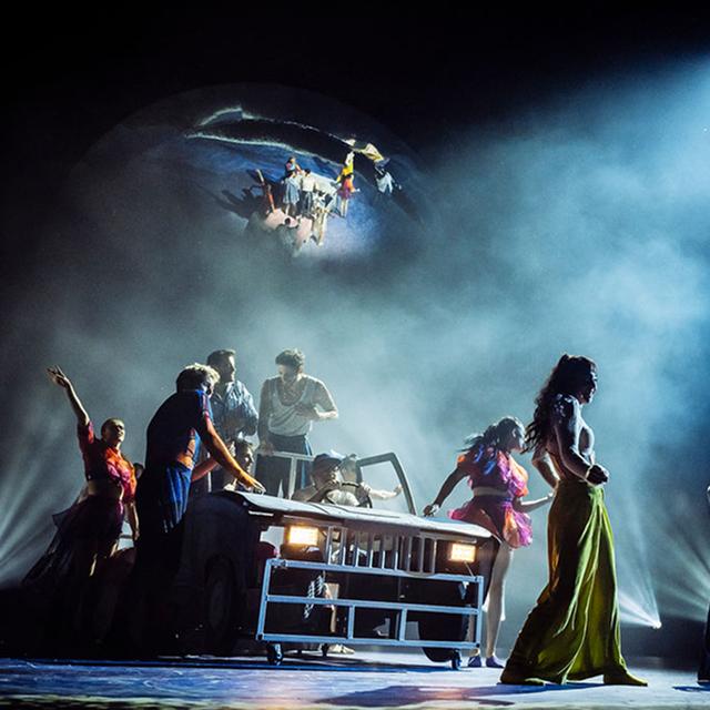 Cirque du Soleil performers gather around a moving stage platform in a dramatic scene filled with mist and theatrical lighting.