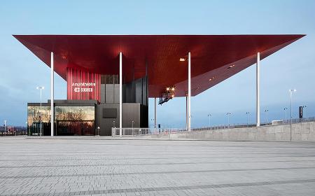 Exterior view of Cogeco amphotheater in trois-Rivière with a striking red roof and open plaza, photographed in daylight.