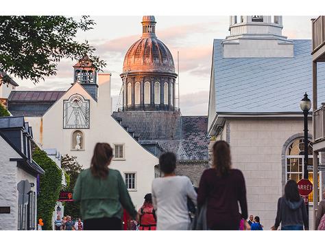 Visitors walk through Trois-Rivières street toward a domed landmark building at sunset.